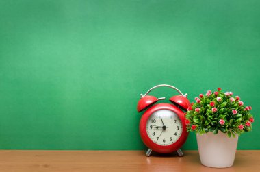 Kırmızı alarm clock ve yapay ağaç ağaç ve yeşil okul yönetimi arka plan üzerinde tencerede. Geri okul kavramı ile arka plan için kopya alanı.