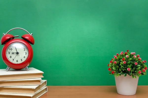 一堆堆书和红色闹钟放在教室里的桌子上 在绿色的学校董事会背景上 回到学校的概念 — 图库照片