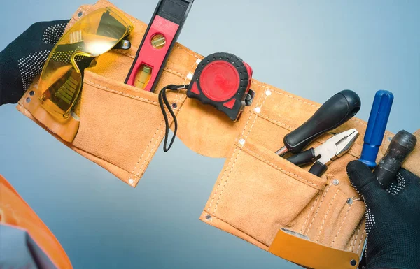 Construction belt with work tools in the worker hands isolated on blue background.