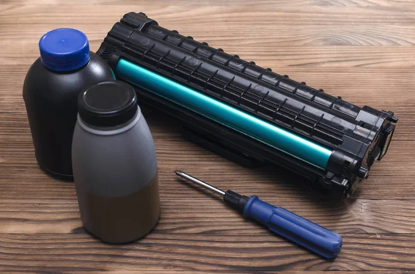 Laser printer cartridge, screwdriver and bottles with toner on the table. Office equipment maintenance concept.