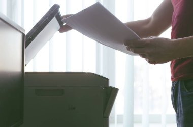 İşadamı belgeleri bir yığın elinde tutan ve yazıcı veya tarayıcı ile çalışıyor. Office evrak kavramı.