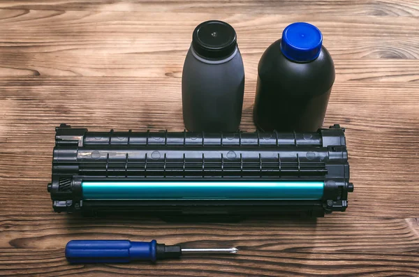 Laser printer cartridge, screwdriver and bottles with toner on the table. Office equipment maintenance concept.