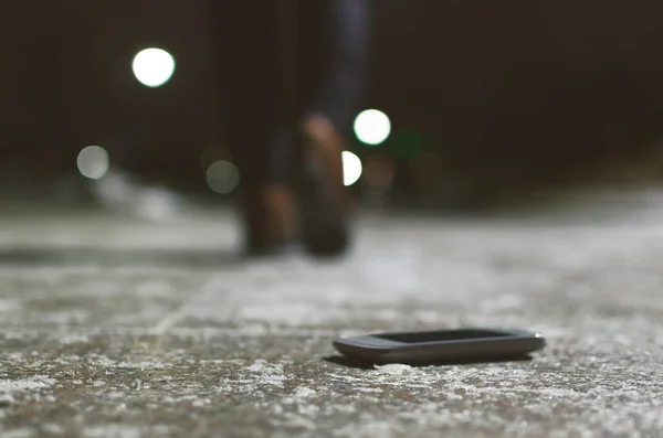 Lost mobile phone dropped from a woman pocket on the night footpath and is walking away silhouette of woman.