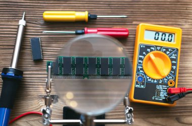 Retro bellek modülü çipi aracılığıyla Büyüteç lehimleme stand ve multimetre, tornavida ve havya teknisyen mühendis tablo arka plan üzerine monte. 