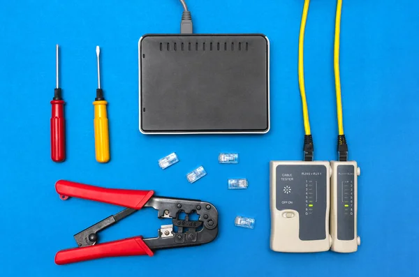 Cripmer tool, network cable tester and a switch router isolated on the blue background. Network maitenance concept.