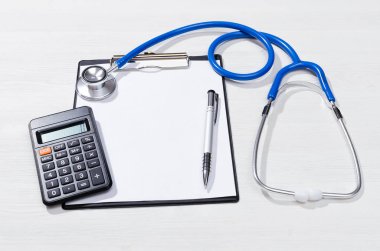 Tıbbi sigorta hesaplama mockup. Tedavi formu maliyetin hesaplanması. Maliyet kadar sahte ilaçların. Boş kağıt sayfası, stetoskop ve beyaz ahşap masa arka plan üzerinde hesap makinesi.