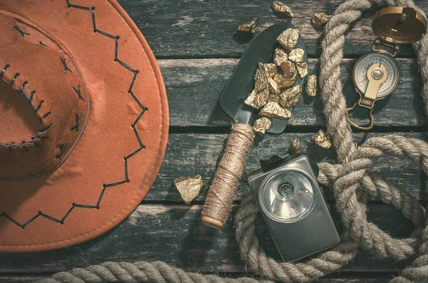 Compas, gold nuggets on the spade, rope and vintage flashlight on the aged wooden table background. Treasure hunter or goldminer concept.