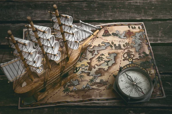 Pirate ship, treasure map and a compass on a wooden table background.