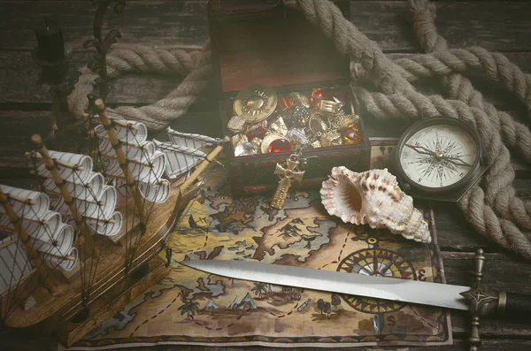 Pirate ship, treasure map, treasure chest full of gold and a compass on a wooden table background.