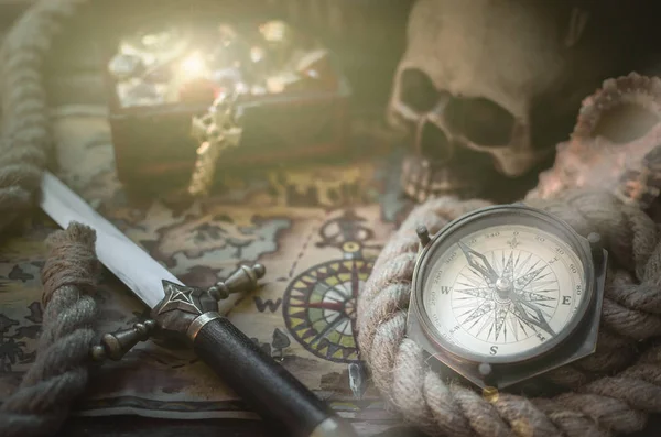 Pirate treasure map, treasure chest full of gold, compass, mooring rope and a sword on a wooden captain table background.