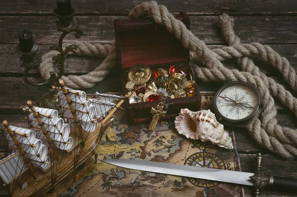 Pirate ship, treasure map, treasure chest full of gold and a compass with dagger on a wooden captain table background.