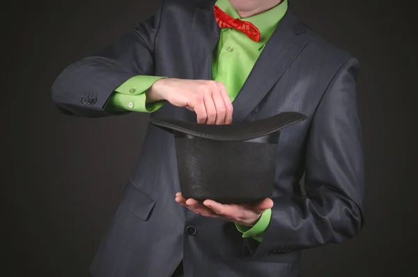 The magician is performing a magic trick with his bowler hat in his hands on a black background.