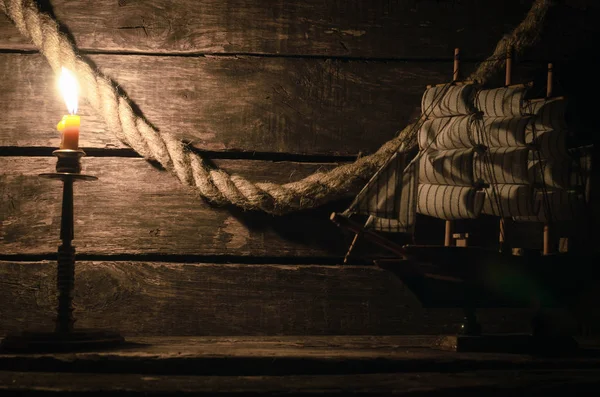 Ship, mooring rope and burning candle on the wooden table. Sea travel concept background. Pirate.