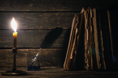 Quill'in kalem inkpot ve yazar Resepsiyon arka plan üzerinde yanan mum ışığında kitap yığını. Eğitim kavramı.