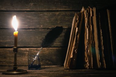 Quill'in kalem inkpot ve yazar Resepsiyon arka plan üzerinde yanan mum ışığında kitap yığını. Eğitim kavramı.