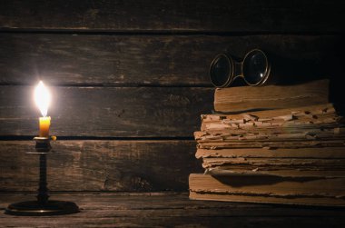 Dürbün, kitaplar ve ahşap masa arka plan kopya alanı ile üzerinde yanan muma yığını. Seyahat veya macera kavramı.