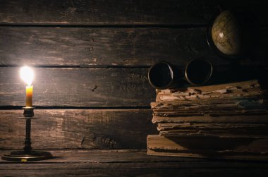 Dürbün, küre, kitaplar ve ahşap masa arka plan kopya alanı ile üzerinde yanan muma yığını. Seyahat veya macera kavramı.