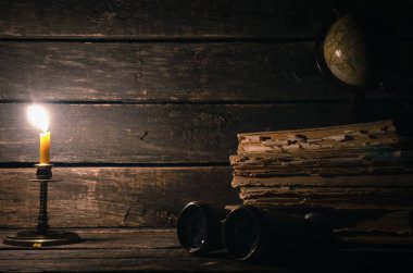 Dürbün, küre, kitaplar ve ahşap masa arka plan kopya alanı ile üzerinde yanan muma yığını. Seyahat veya macera kavramı.