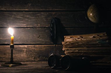 Dürbün, küre, kitaplar ve tüy yığını kopya alanı ile ahşap masa arka plan üzerinde mum yanan ışığında bir inkpot kalem. Seyahat veya macera kavramı.