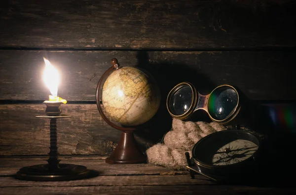 Travel or adventure background. Binoculars, globe, compass and mooring rope on the ship captain table in the light of burning candle.