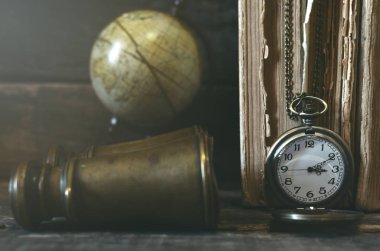 Seyahat ya da macera kavramı geçmiş. Cep saati, dürbün, küre ve maceraperest masada kitap yığını.