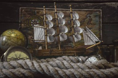 Sailboat, compass, globe, binoculars, pocket watch and mooring rope on a wooden captain table background. Sea travel concept.