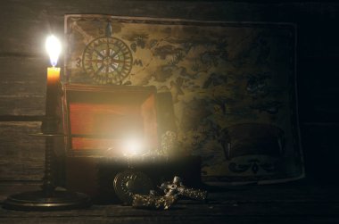Pirate map and treasure chest with a gold on a pirate captain table in the light of burning candle background.