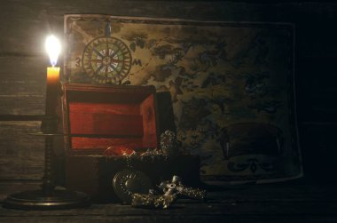Pirate map and treasure chest with a gold on a pirate captain table in the light of burning candle background.