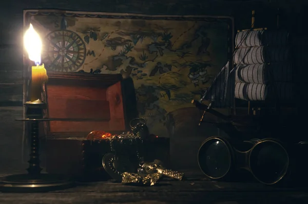 Pirate map, binoculars and treasure chest with a gold on a pirate captain table in the light of burning candle background.