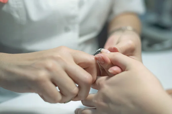 Manicurist master is cutting the length of nails with nail clippers. Nail care concept.