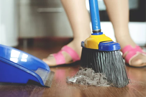 Woman is sweeping the floor by a sweeping brush from a dust.