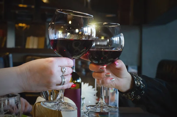 People are clinking wine glasses with red wine and talking a celebration toasts.