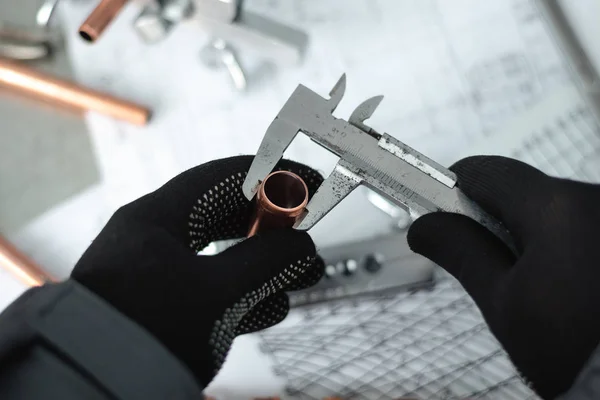 Engineer is holding in hands a brass pipe and is measuring a diameter by a calipers. Pipework.