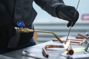 Worker is soldering a pipe by a blow lamp on a factory workbench background. Pipework. clipart