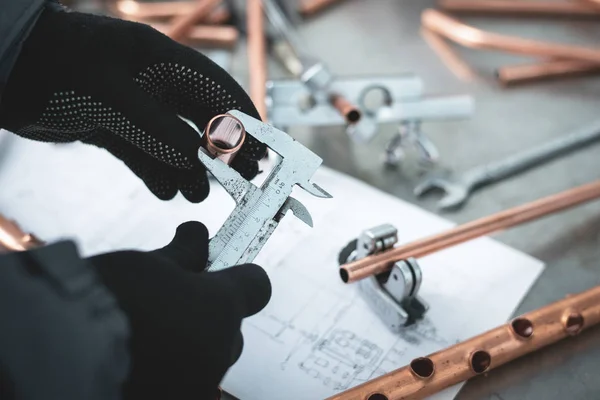 Engineer is holding in hands a brass pipe and is measuring a diameter by a calipers. Pipework.