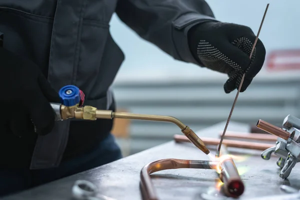 Worker is soldering a pipe by a blow lamp on a factory workbench background. Pipework.