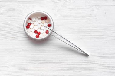 Beyaz ve kırmızı tabletler ve Beyaz ahşap masa arka plan üzerinde bir Forseps ile jar. Tıp arka plan.