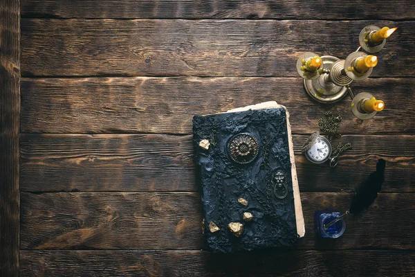 Antik sihirli kitap, cep saati ve kopya alanı bir ahşap masa zemin üzerine mum yanan ışığında siyah tüy kalem. Büyü kavramı kitap.