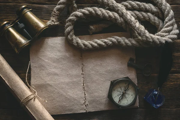 Blank traveler notebook, compass, binoculars, mooring rope and inkpot with a quill pen on a wooden table background mockup. Adventurer notes.