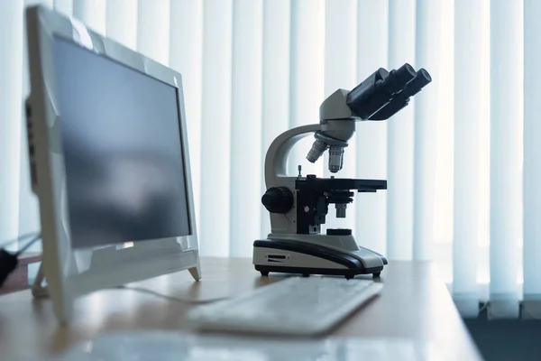 Microscope and a personal computer on a table in a laboratory on a window light background.