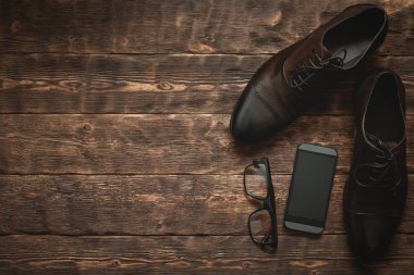 Hareket eden telefon ile boş bir ekran, gözlük ve kopya alanı bir kahverengi ahşap zemin zemin üzerine şık bir ayakkabı gibi işadamı aksesuarları.