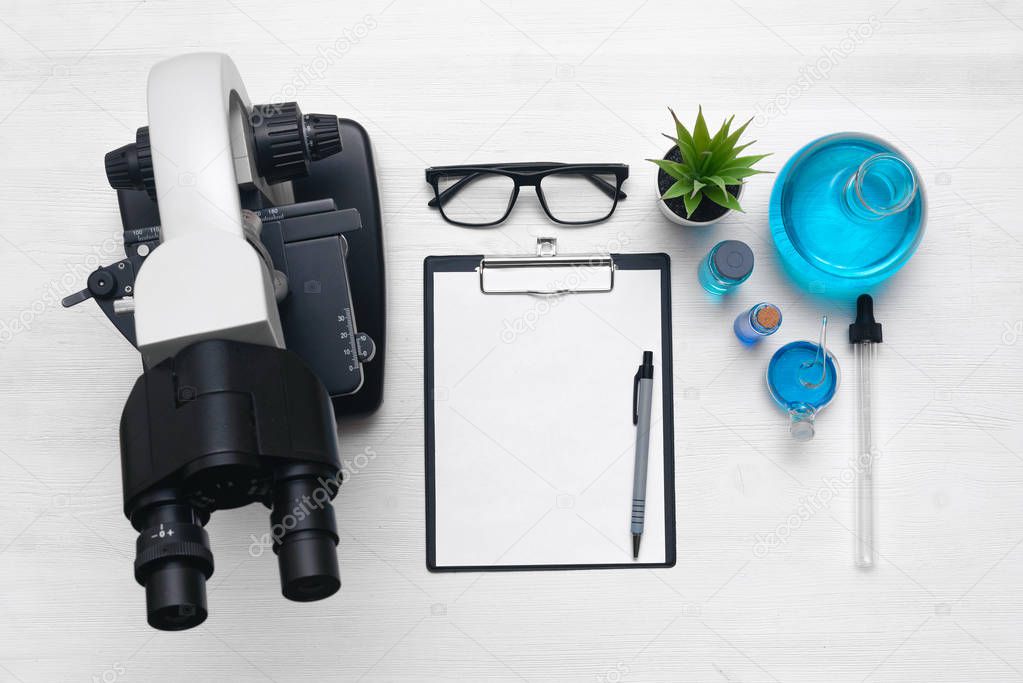 Laboratory table with a blank paper sheet of researching results, microscope and a chemical reagent liquids background with copy space. Medical examination mock up.