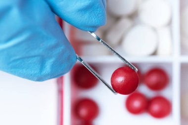 Bir kırmızı tıbbi tablet doktor elinde bir forseps. Tıp, eczacılık, eczane arka plan.