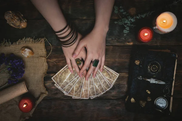 Tarot cards, magic book and fortune teller hands on a wooden table background. Future reading concept. Divination.