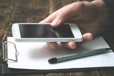 Bir işadamı olarak boş ekran cep telefonunuzla bir office tablo arka plan üzerinde eller. Bize ulaşın.