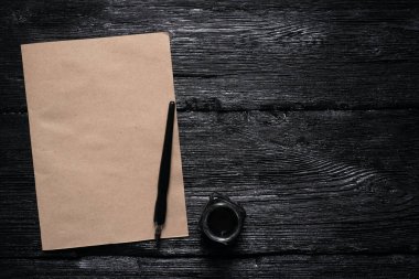 Fotokopi alanı, tüy kalemi ve siyah tahta bir masa üzerinde mürekkep hokkası olan kahverengi boş kağıt sayfa..