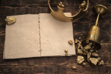 Boş bir sayfa kitabı, altın bir taç ve ahşap bir masa arkasında altın dolu bir kadeh..