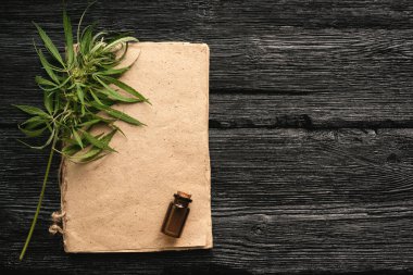Kenevir cbd yağ tarifi boş kitap, bir kopya alanı, bir şişe cbd yağ ve siyah ahşap masa arka planında yeşil yapraklar.