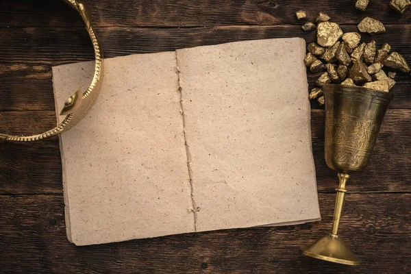 Boş bir sayfa kitabı, altın bir taç ve ahşap bir masa arkasında altın dolu bir kadeh..