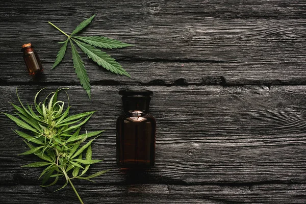 Cannabis essential oil in the bottle and a green stem with leaves on a black wooden table background.